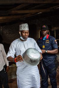 Hon Ige holding a finished product and ikoko Irin Fabricator's shop in Saki